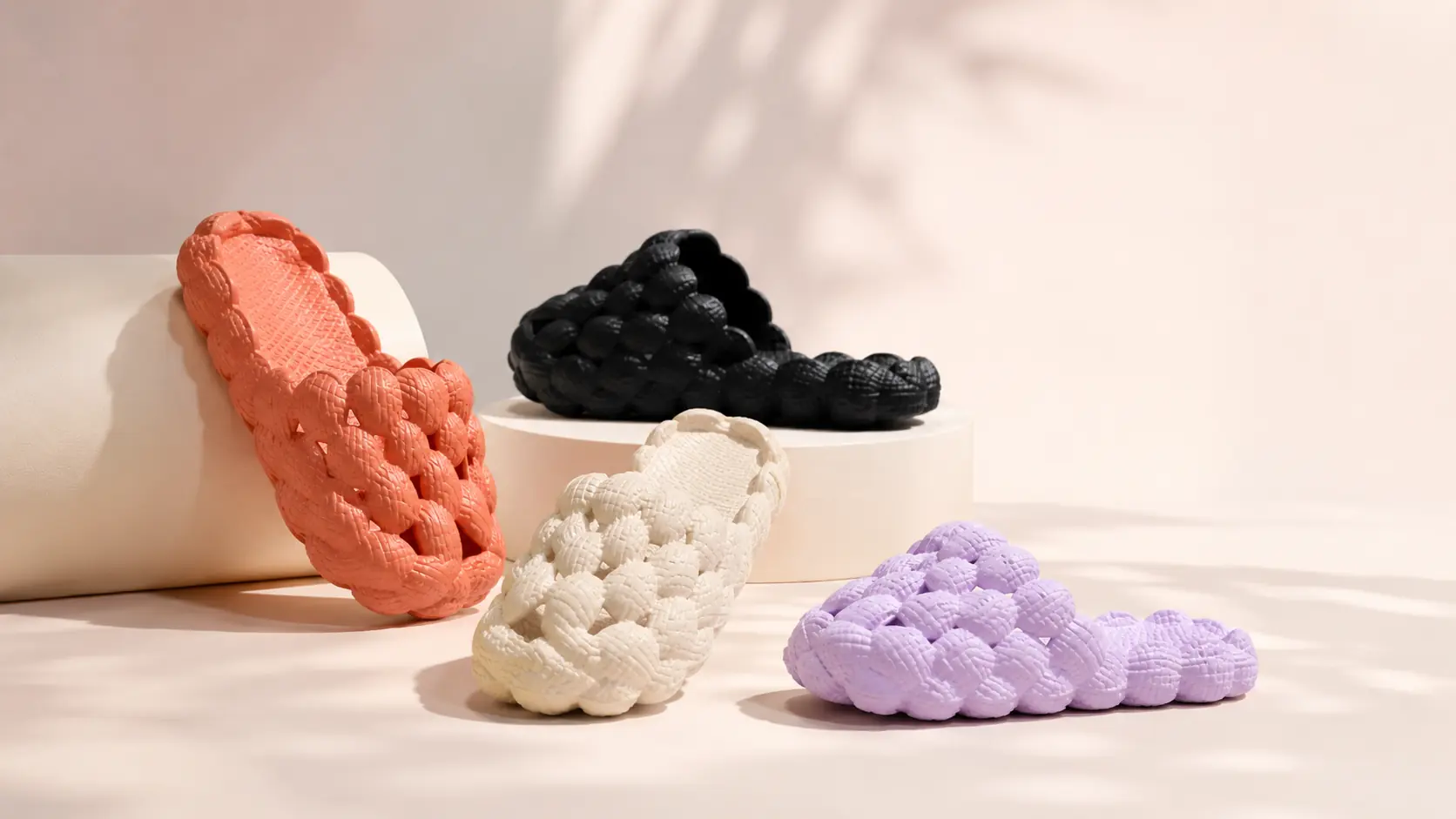 Coral, black, cream and lilac woven cloud slides displayed in a warm editorial studio